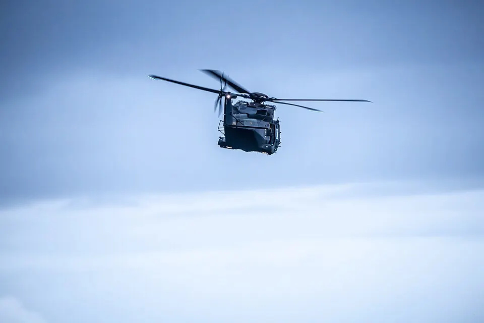 An NH90 military helicopter flying at dusk under heavy cloud.