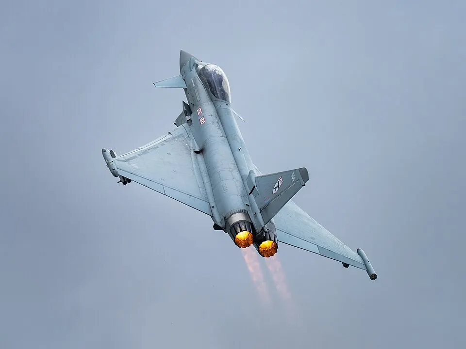 A Eurofighter Typhoon climbing steeply with both afterburners lit against a grey sky.